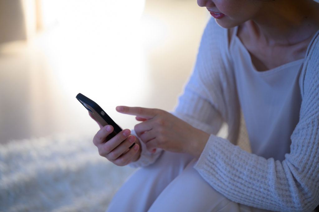 ベッドで電話をとろうとする女性のイメージ