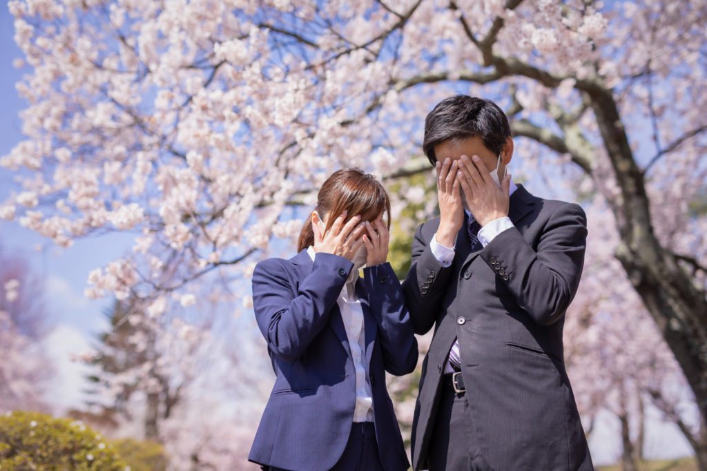 桜の下で顔を手で抑える新入社員